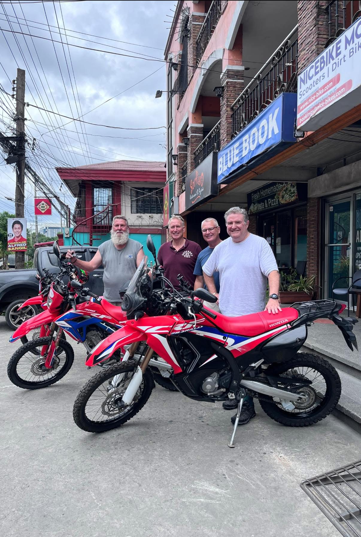 Four customers with red dual-sport motorcycles outside NiceBike